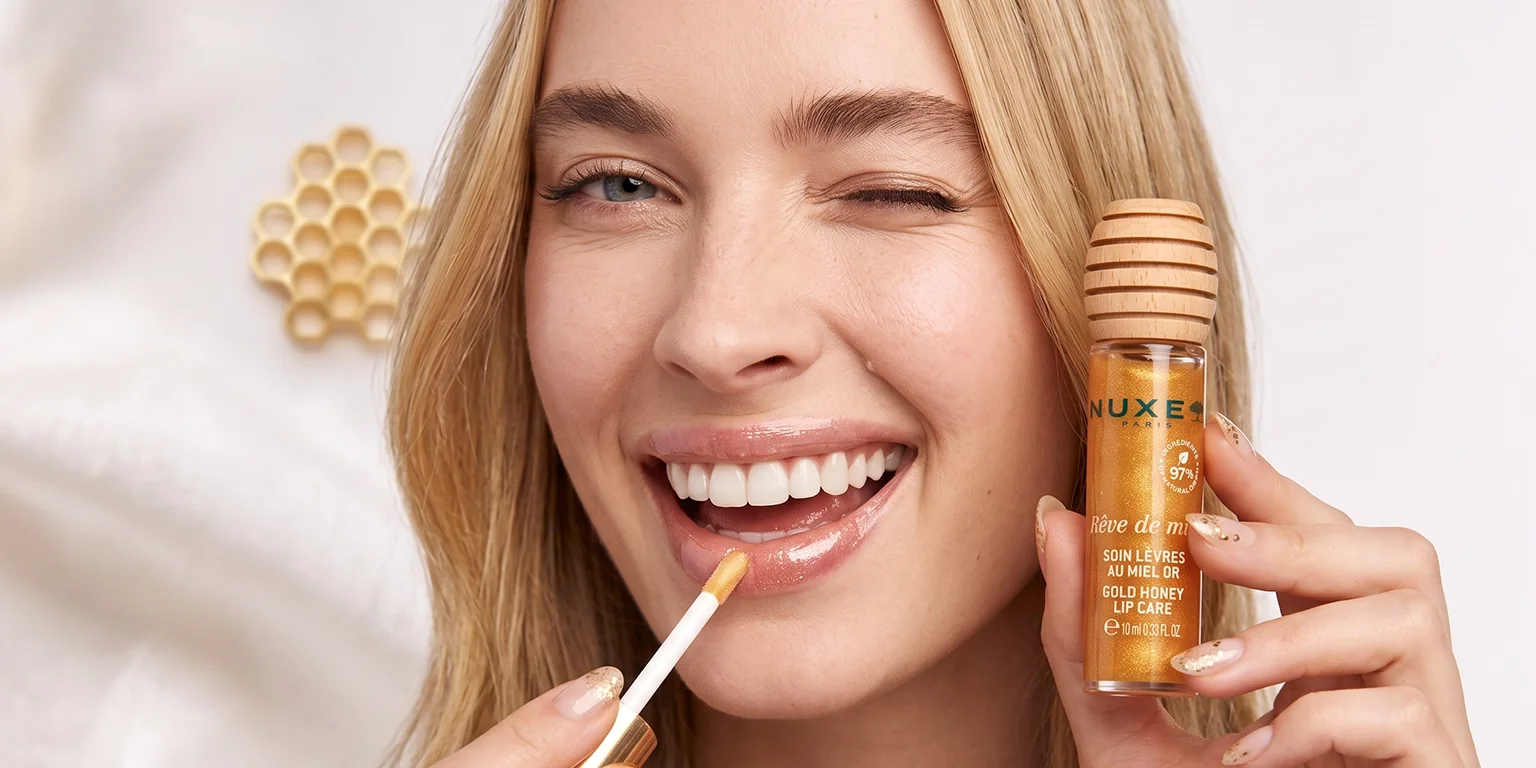 Cómo aplicar el Tratamiento Labial con Miel Gold de NUXE para dar brillo Aplicación del aceite labial NUXE Rêve de Miel Gold con el aplicador de espuma, con un panal de miel al fondo