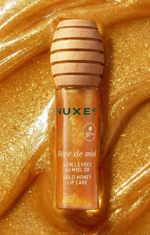 Envase del Tratamiento Labial con Miel Gold de NUXE sobre una textura de miel dorada con brillos