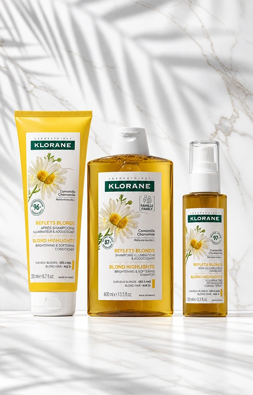 Set Klorane Camomila Reflejos Dorados: champú, acondicionador y spray iluminadores para cabello rubio, sobre mármol