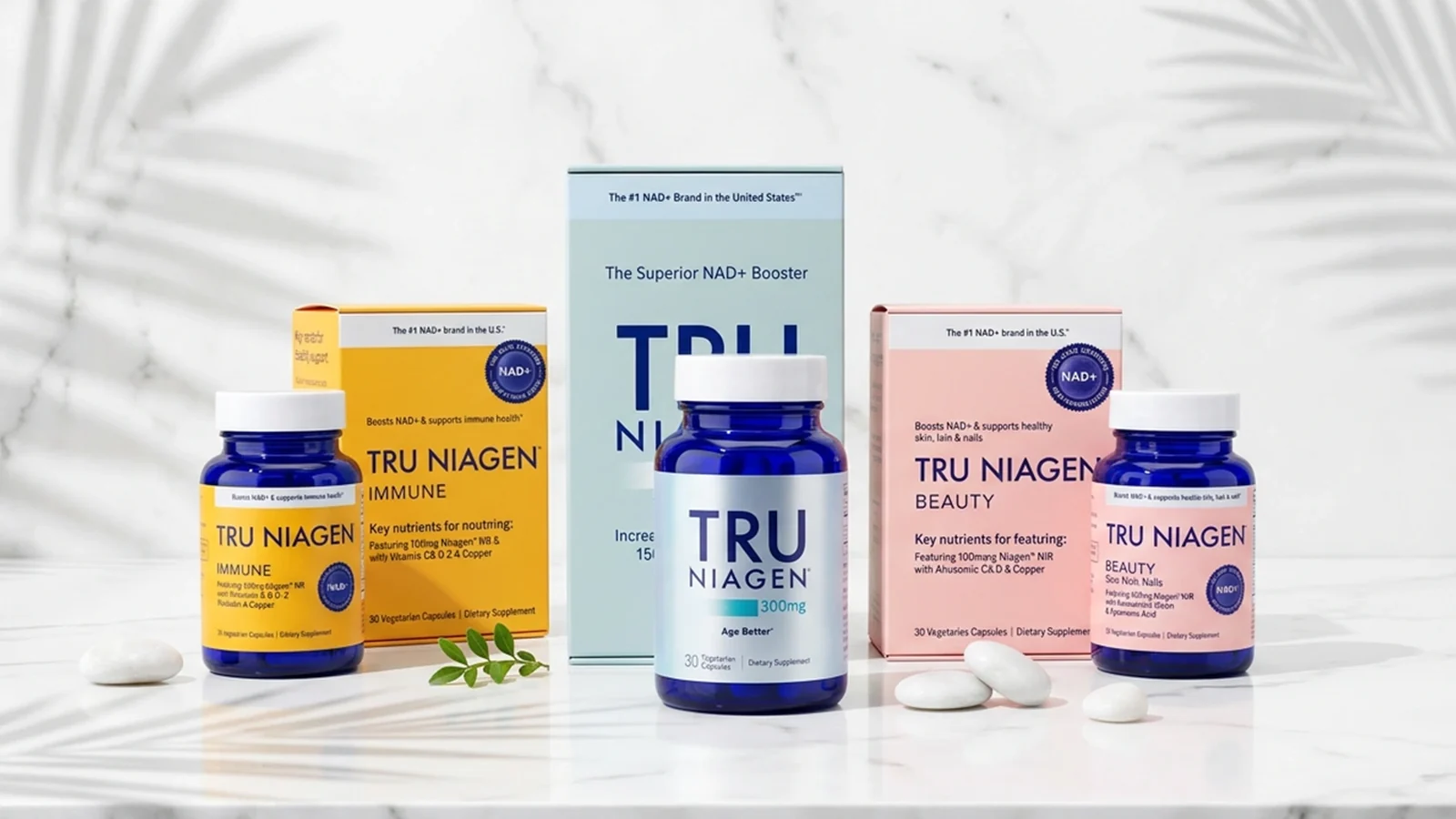 Las tres fórmulas de Tru Niagen —300 mg, Immune y Beauty— con sus estuches y frascos de cápsulas sobre mármol